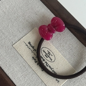 Detail of a shiny rose red acetate bow pendant on a high-elastic black hair tie