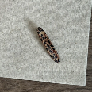 Detailed top view of leopard print oval hair clip on a natural linen and wood background