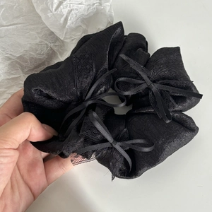Close-up of black satin scrunchie featuring elegant lace trim and a delicate bow detail