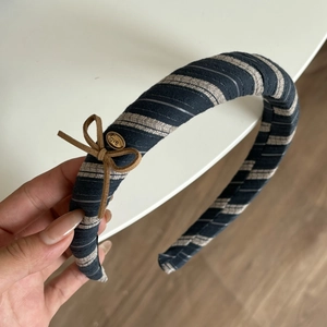 Detail of striped fabric headband featuring a brown suede bow and gold 'love' charm