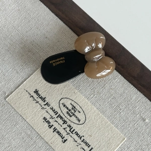 Detailed close-up of handmade acetate bow hair clip with gold lettering on beige fabric
