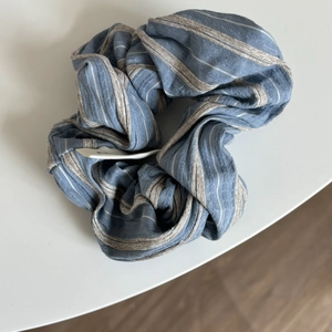 Detailed view of blue and beige striped fabric scrunchie with cotton texture and tag