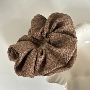 Detailed close-up of brown herringbone tweed scrunchie on white porcelain shell plate