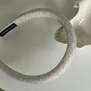 Detail of oatmeal grey knitted hairband featuring a black and white hand made woven label