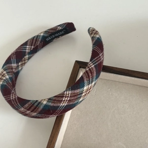Macro detail of a thick plaid headband showing vintage burgundy fabric and a handmade label