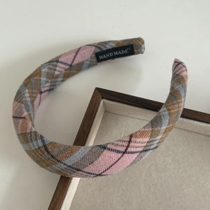 Close-up of a pink plaid padded headband with a handmade label on a wooden tray