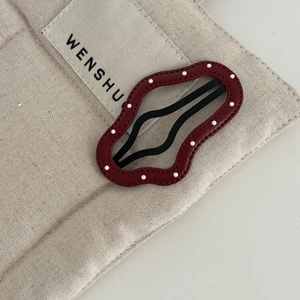 Close-up of burgundy wavy leather hair clip with white dots on beige canvas background