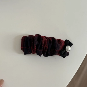 Detail of red plaid fabric hair scrunchie with black bow and white pearl accent