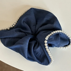Macro detail of dark blue denim scrunchie with white pearl trim and textile texture