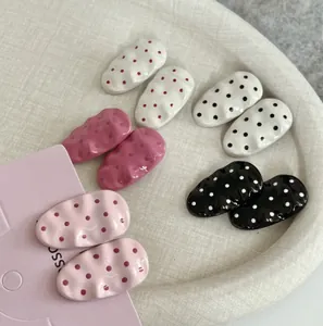 Detailed view of pink and black polka dot metal hair clips in a textured beige tray