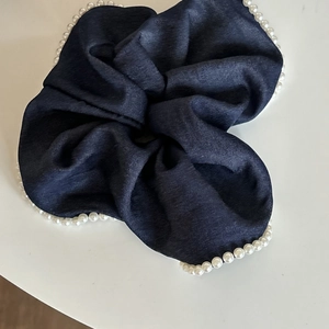 Detailed view of dark blue denim scrunchie with elegant white pearl beaded edge trim