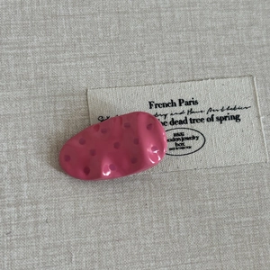 Pink polka dot oval metal hair clip with a sweet wavy texture on beige canvas background