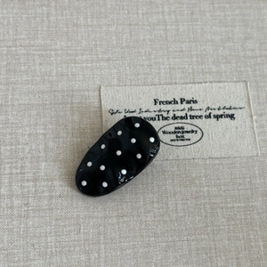 French vintage style black hair clip with white polka dots on a textured beige fabric