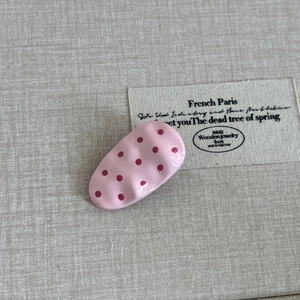 Detailed macro view of a pink polka dot oval hair clip with wavy edges on fabric