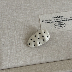 Macro detail of wave-textured hair clip in beige with black polka dots on linen