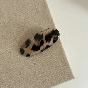 Leopard print oval hair clip made of acetate with a glossy finish on beige fabric