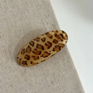 Macro shot of oval leopard print hair clip on linen fabric texture with shiny finish