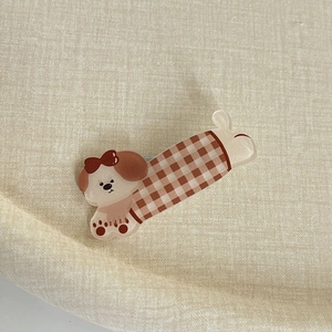 Détail d'une pince à cheveux petit chien avec nœud rouge et motif à carreaux marron