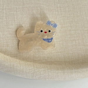 Détail d'une pince à cheveux chat en acétate sur un tissu beige doux et texturé