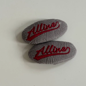 Detail of grey corduroy hair clip featuring red Allure cursive embroidery on white background