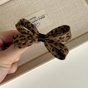 Detail of the leopard print bow hair clip featuring satin fabric texture and classic pattern