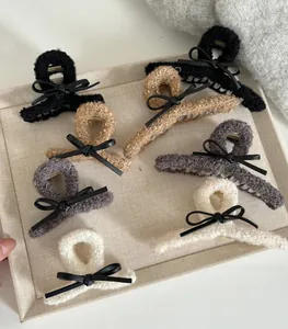 Detail of plush bow claw clips in black, beige, and grey displayed on a linen tray