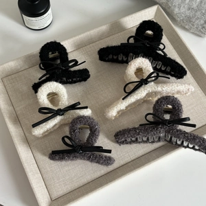 Plush lamb wool claw clips with leather bows in black, white and grey on a beige tray