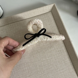 Detailed view of off-white bouclé hair claw clip featuring a delicate black leather bow accent