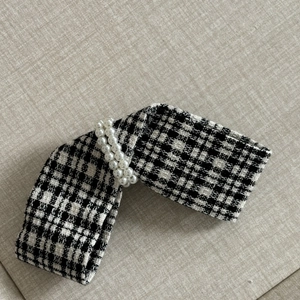 Detailed close-up of plaid bow hair clip featuring tweed fabric and pearl embellishments