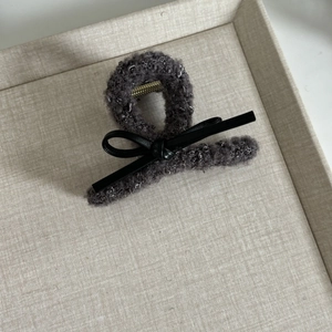 Detail of dark grey faux fur shark clip with leather bow on a beige textured tray