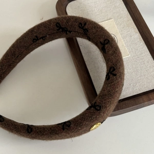 Detail of a brown wool headband featuring black embroidered bows and a gold emblem