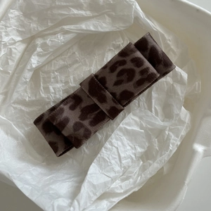 Detail of a leopard print bow hair clip with velvet texture inside a white gift box