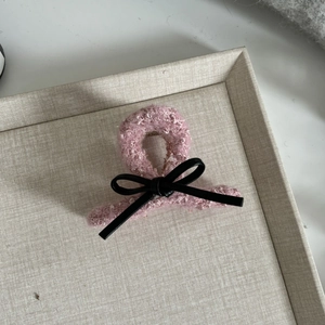 Pink tweed hair claw clip with black leather bow detail on a beige woven tray