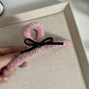 Detail of pink bouclé fabric hair claw clip with black bow and soft textured surface