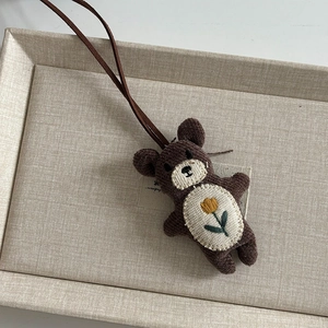 Nahaufnahme einer handgefertigten Plüschbär-Pulloverkette mit Blumenstickerei und Lederband