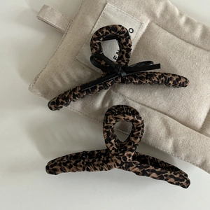 Detail shot of leopard print fabric hair clips with black leather bow accent on beige linen