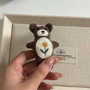 Detail eines braunen Plüschbären-Anhängers mit gelber Tulpenstickerei und Cord-Textur
