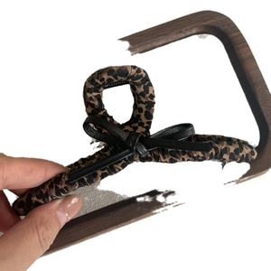 Leopard print fabric hair claw clip with black bow accent shown in hand