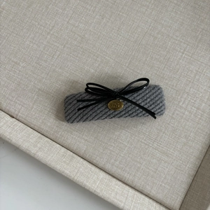 Detail of grey knitted hair clip featuring a black leather bow and gold metal logo charm