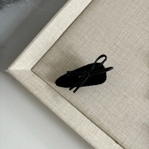 Detail view of a black velvet and faux leather bow hair clip on a beige linen tray