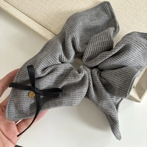 Gray knitted oversized scrunchie with a black bow and gold metal tag for ponytails