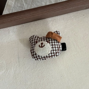 Detail einer braun-karierten Teddybär-Haarklammer mit Schleife auf weichem Stoffhintergrund
