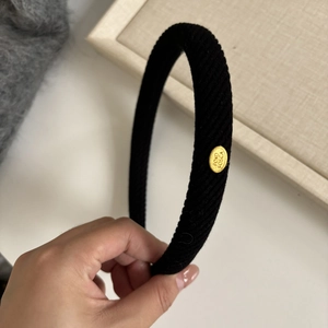 Close-up of black ribbed knit headband featuring a gold oval metal logo charm detail