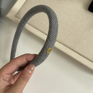 Detail shot of a grey knitted headband with a gold logo plate and ribbed fabric texture