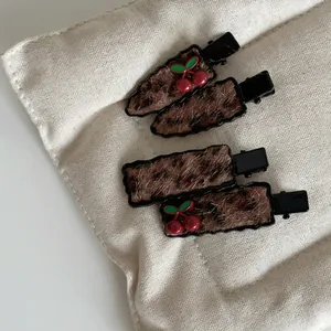 Set of four leopard print plush hair clips with cherry charms on a quilted base