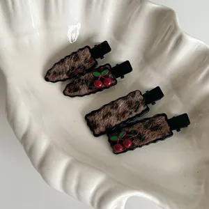 Set of four plush leopard print hair clips with cute cherry accents on a white shell tray