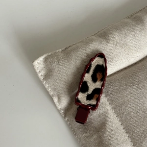 Détail d'une pince à cheveux léopard avec base bordeaux sur tissu beige texturé