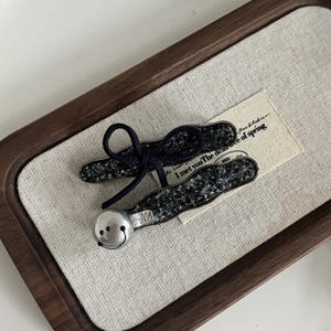 Dettaglio di fermagli in tweed con smiley argento e fiocco blu su un vassoio rustico