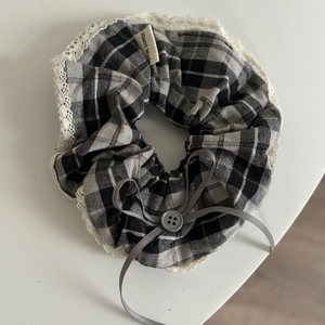Detail of grey plaid scrunchie with white lace trim, grey bow, and button detail