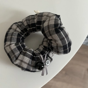 Detailed shot of grey plaid scrunchie with silk ribbon bow and decorative button accent